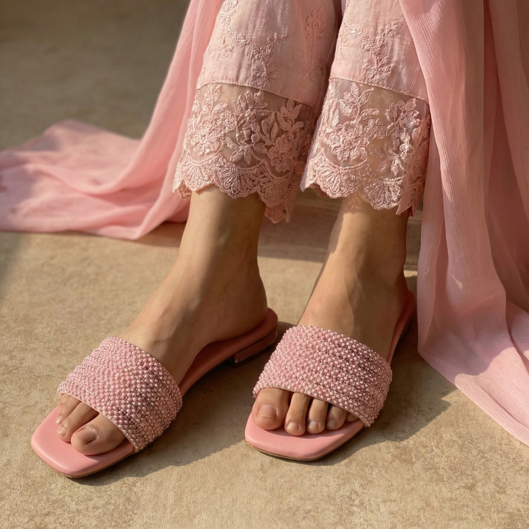Pink beaded fancy flat slippers paired with a soft pink embroidered outfit, styled for an elegant casual look.